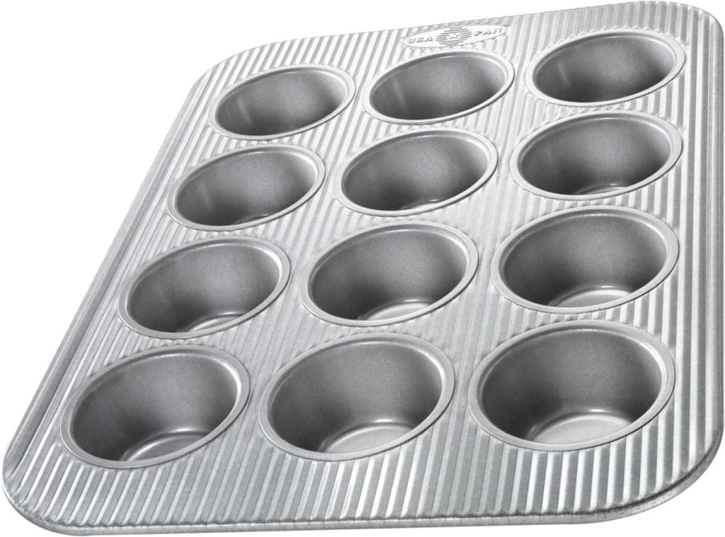 Twelve-cup metal muffin pan with a ribbed surface, ideal for baking treats like kouign-amann, viewed at an angle.
