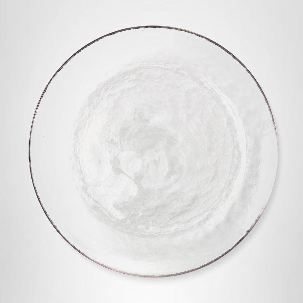 A round, clear glass plate with a subtle swirl pattern is centered on a plain white background, perfect for showcasing your favorite dinner party recipes.