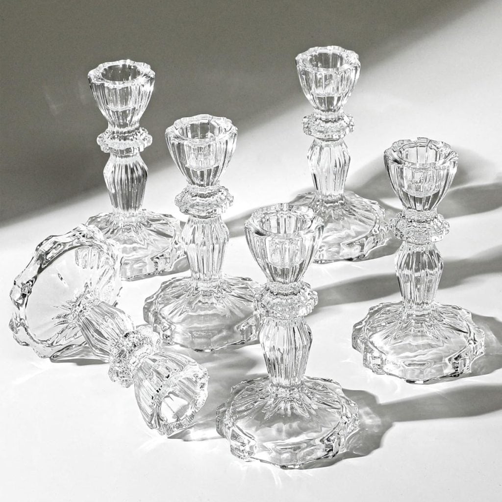Seven clear glass candlestick holders are arranged on a white surface—perfect décor inspiration for your next gathering as you browse dinner party recipes. Two lie on their sides, while five stand upright, adding elegance to any table.