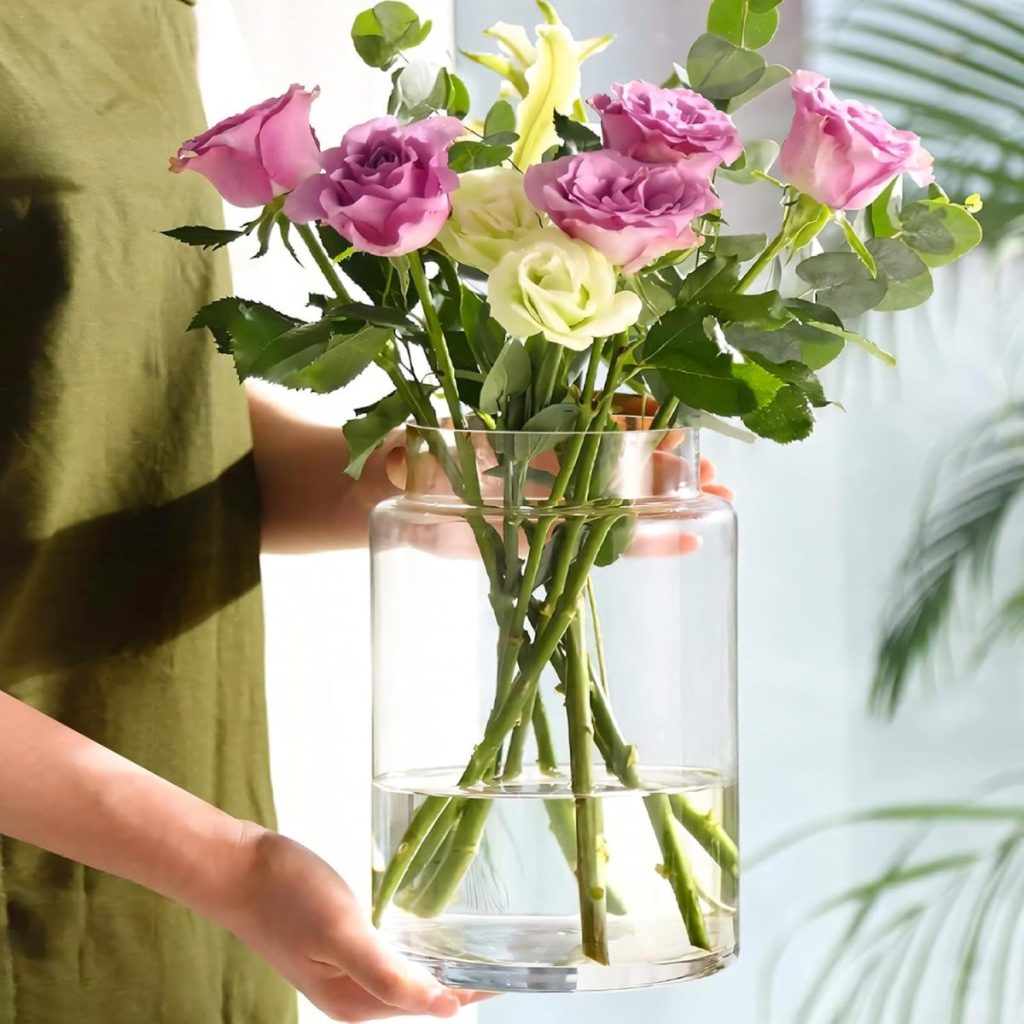A person in a green shirt holds a glass vase with water containing light purple and white roses and green foliage, perfect for charming Outdoor Table Decor.
