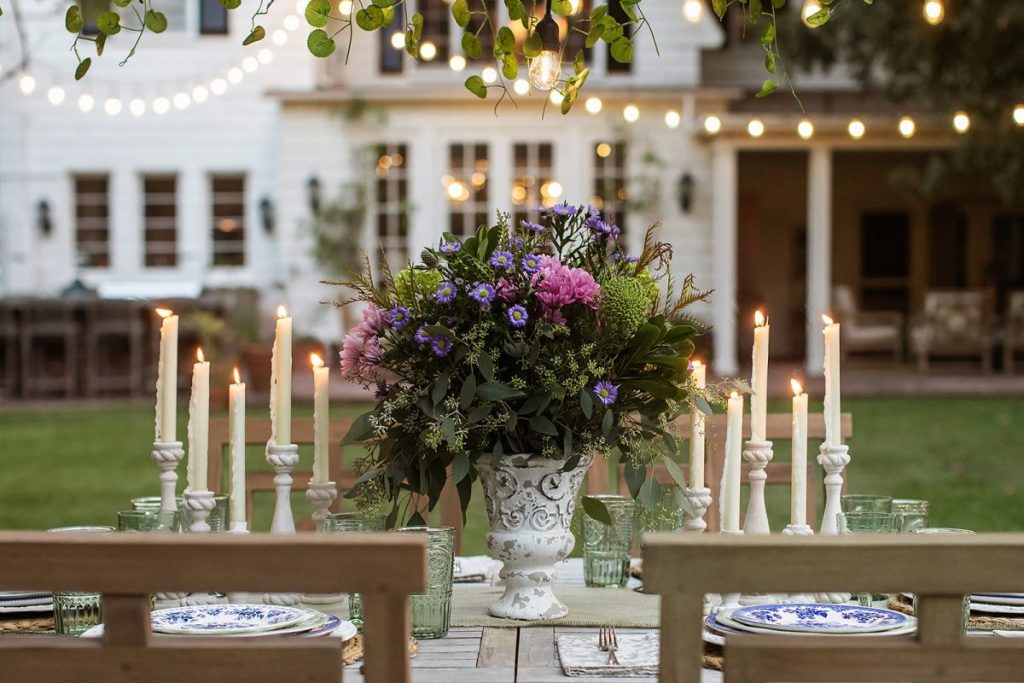 outside table with large was and flowers, candles, and plates