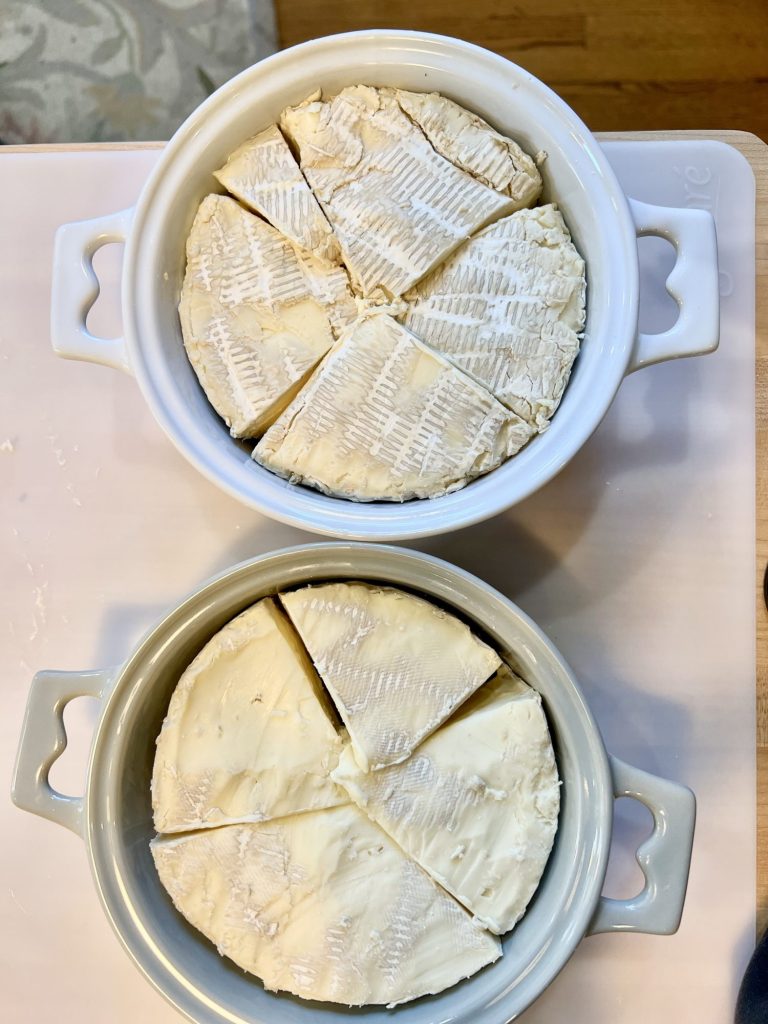 overhead photo of two brie baking dishes filled with brie cut into triangles to fit into the dish