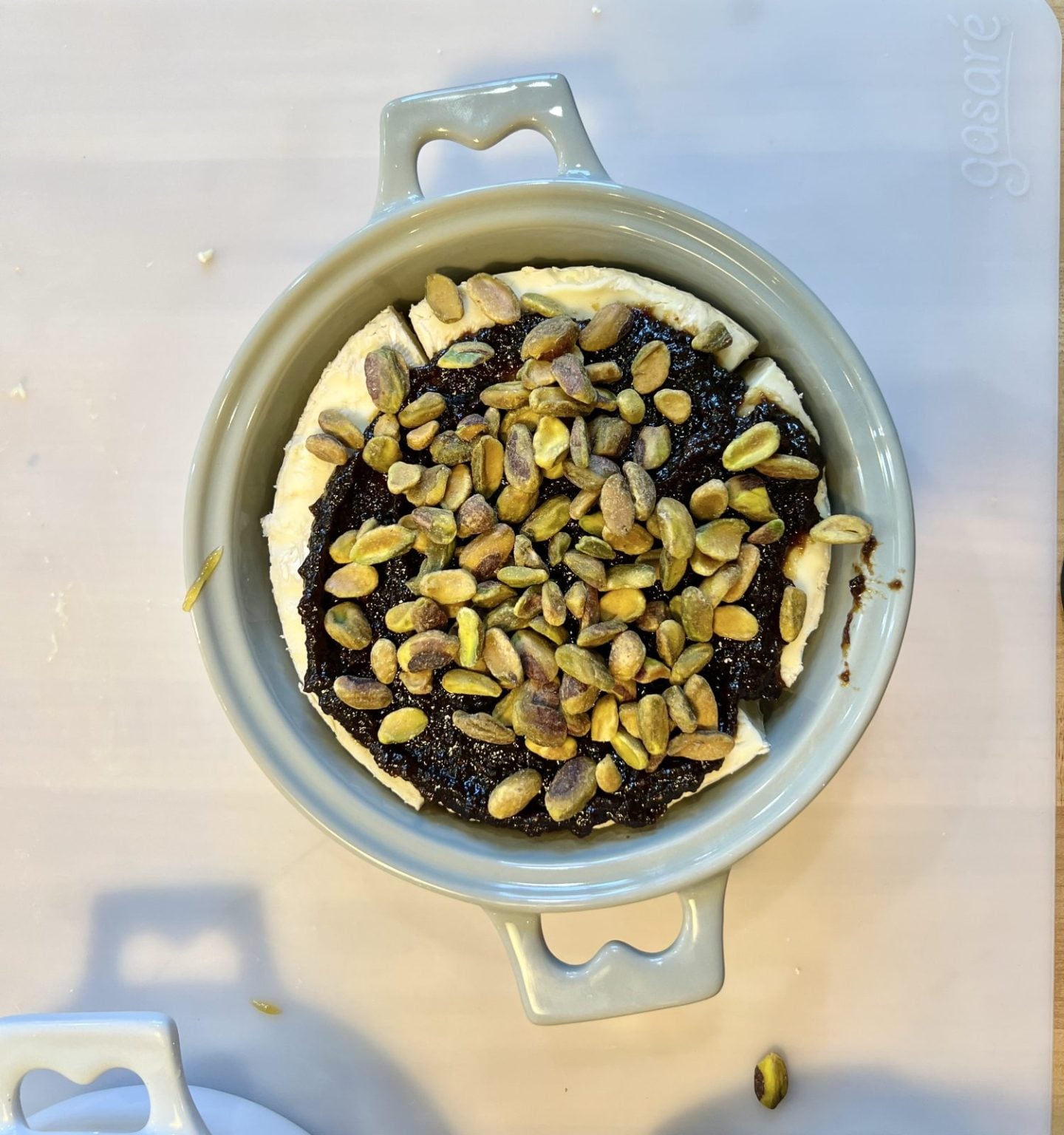 Brie baker filled with brie, fig jam and roasted pistachios, ready to go into the oven