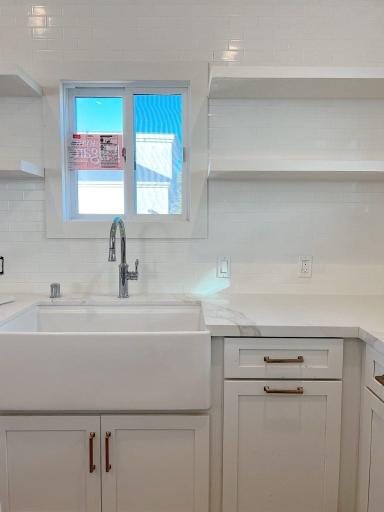 white kitcehn with farmhouse sink, quarts countertops. window, shelves, and new faucet.