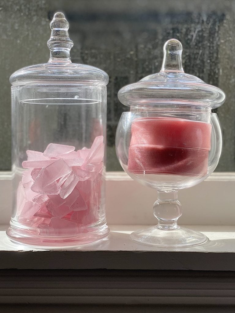 Pink glass and pink ribbon in two glass apothecary jars.