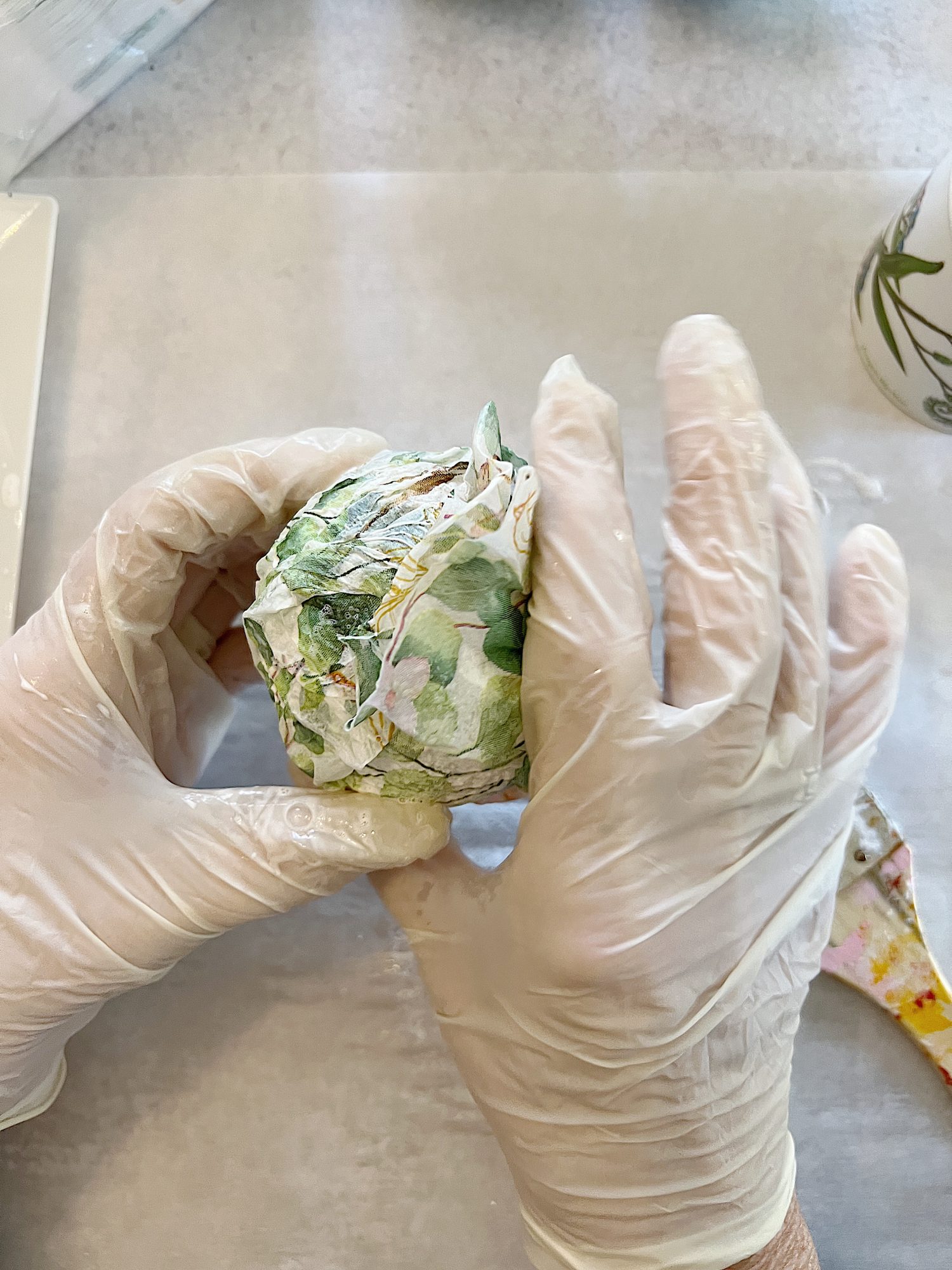 covering small styrofoam balls with paper napkin with green eucalyptus design and mod podge glue