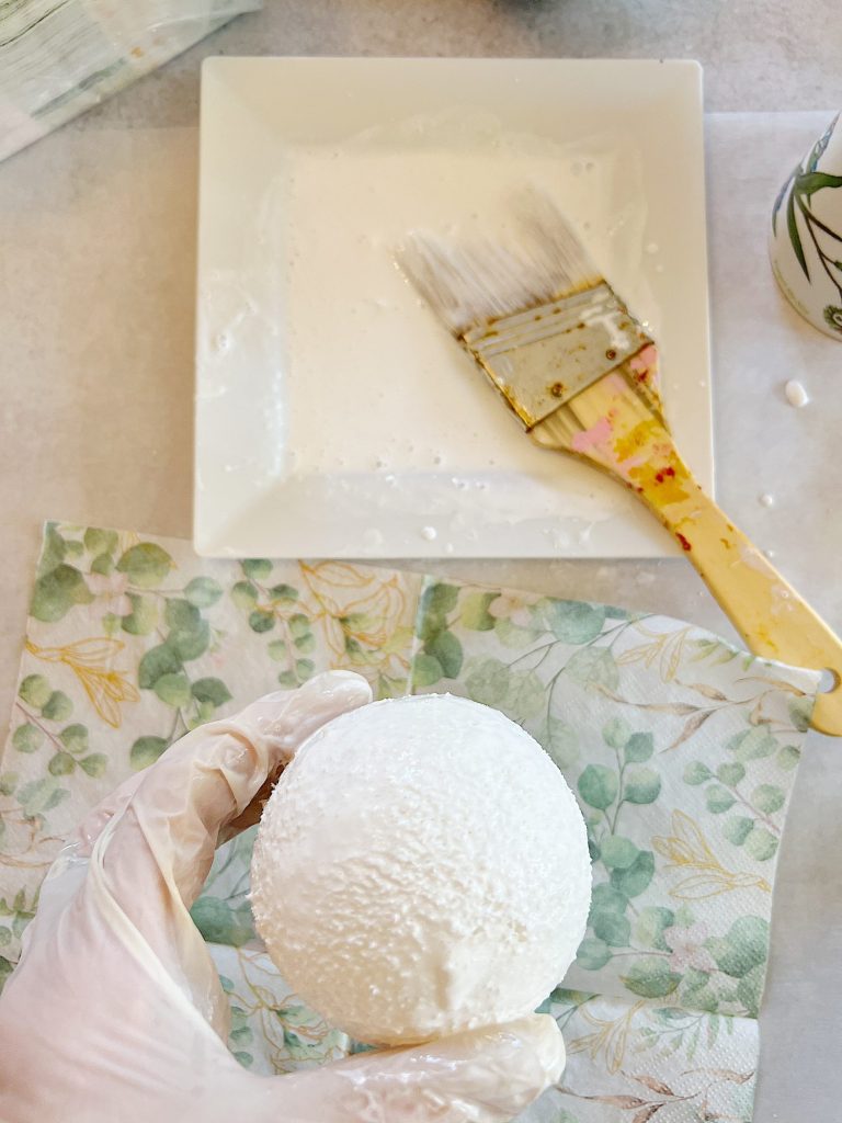 covering small styrofoam balls with paper napkin with green eucalyptus design and mod podge glue