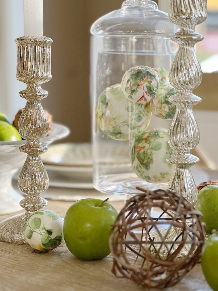table with green palce settings and apothecary jars with green apples, wood balls, and decor balls