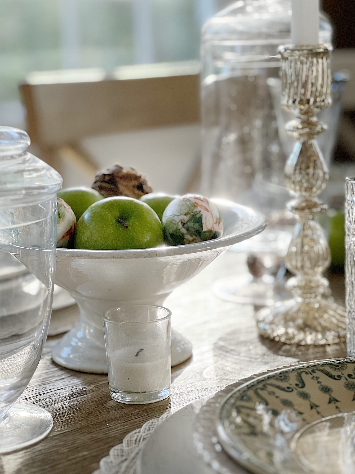 table with green palce settings and apothecary jars with green apples, wood balls, and decor balls