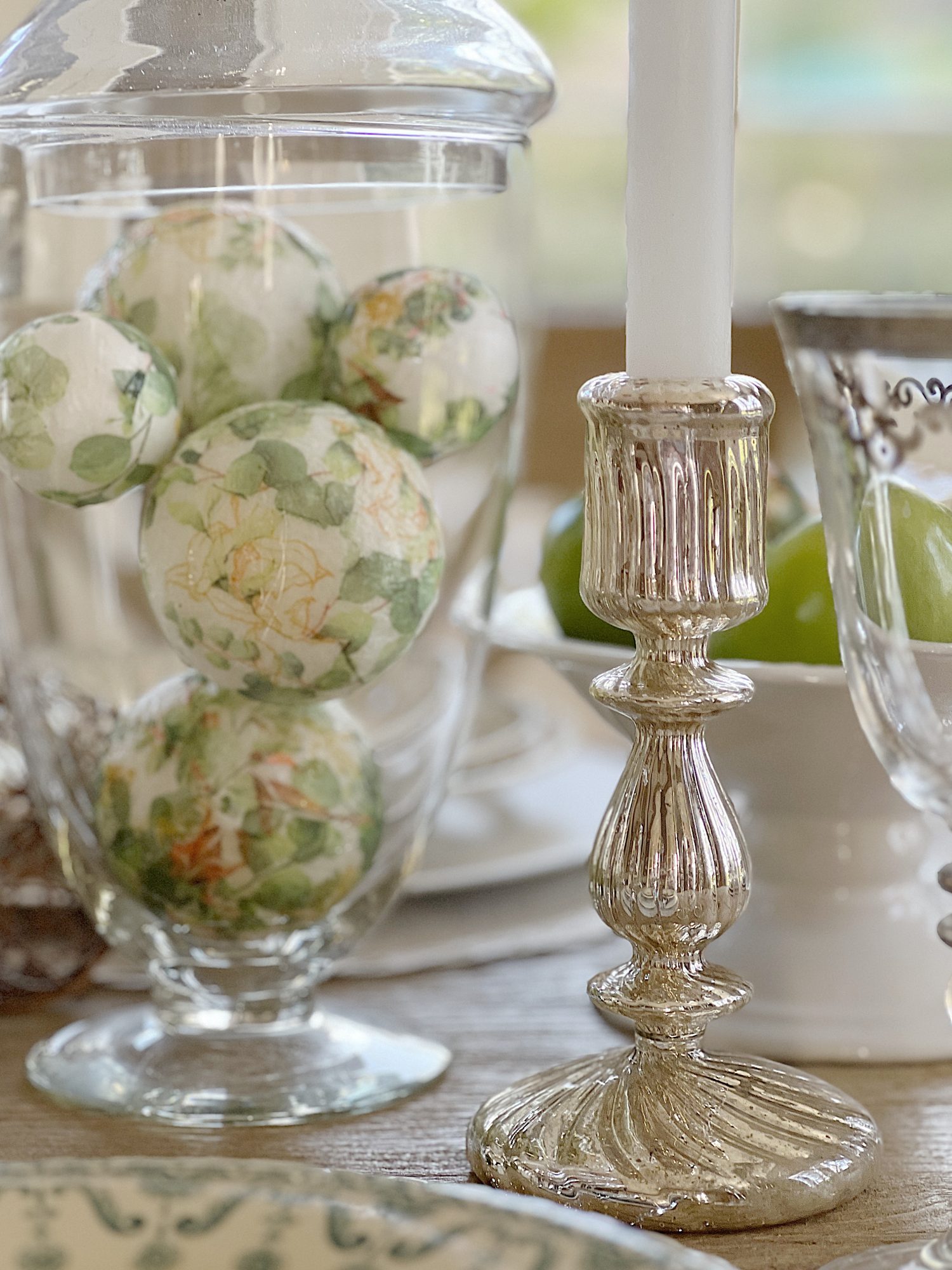 table with green palce settings and apothecary jars with green apples, wood balls, and decor balls