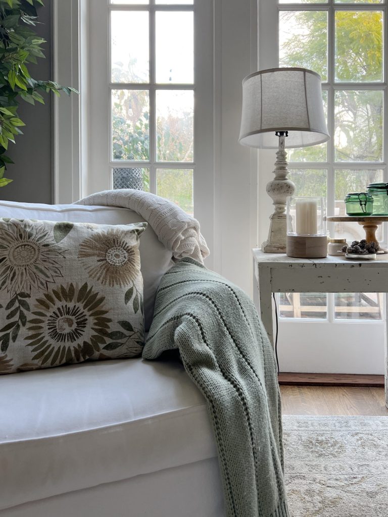 a sage and cream throw on top of a white chair with a floral pillow