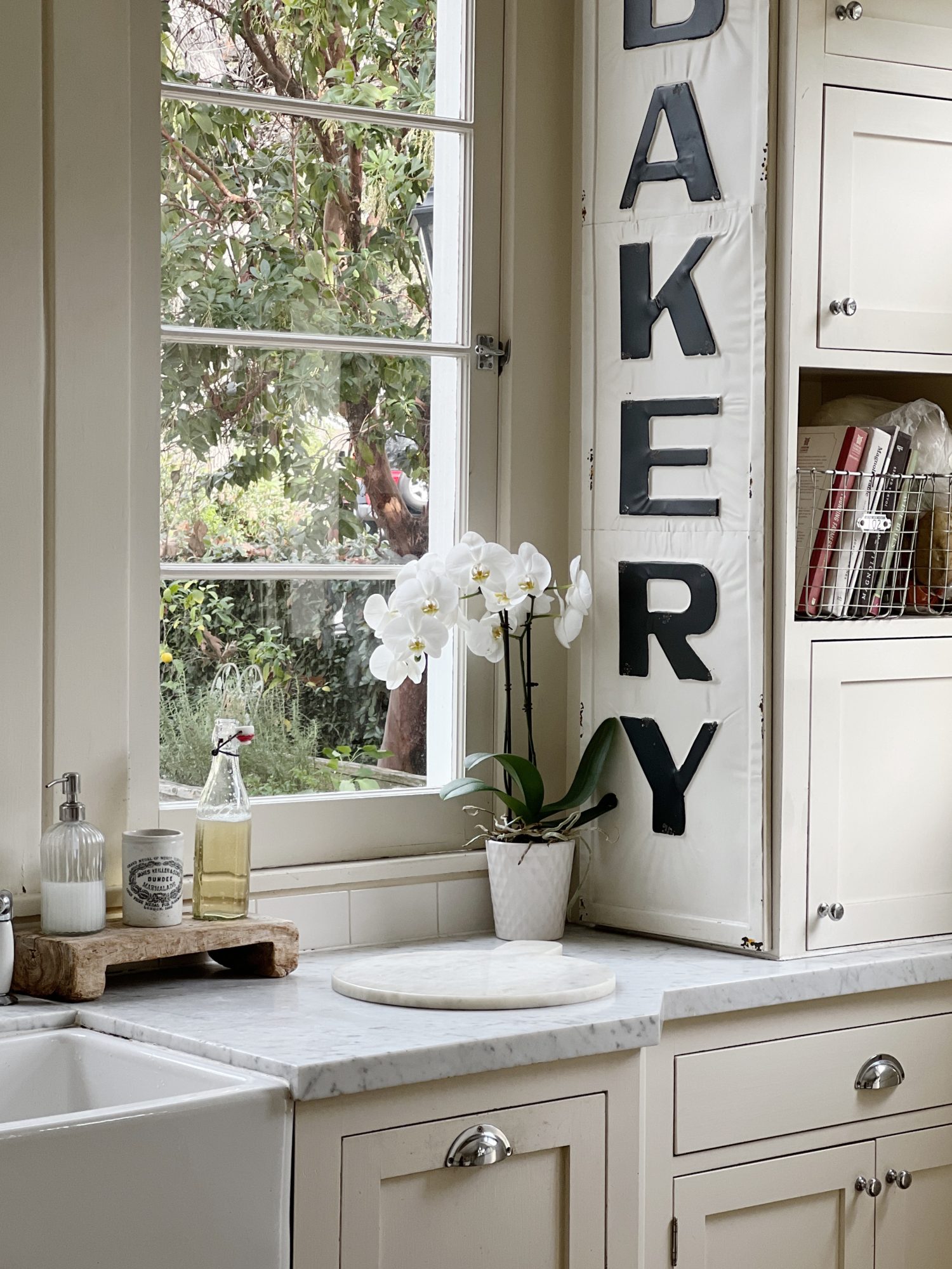 a white kitchen with windows and an island with a bowl with apples, a cutting board and wreaths in the windows.
