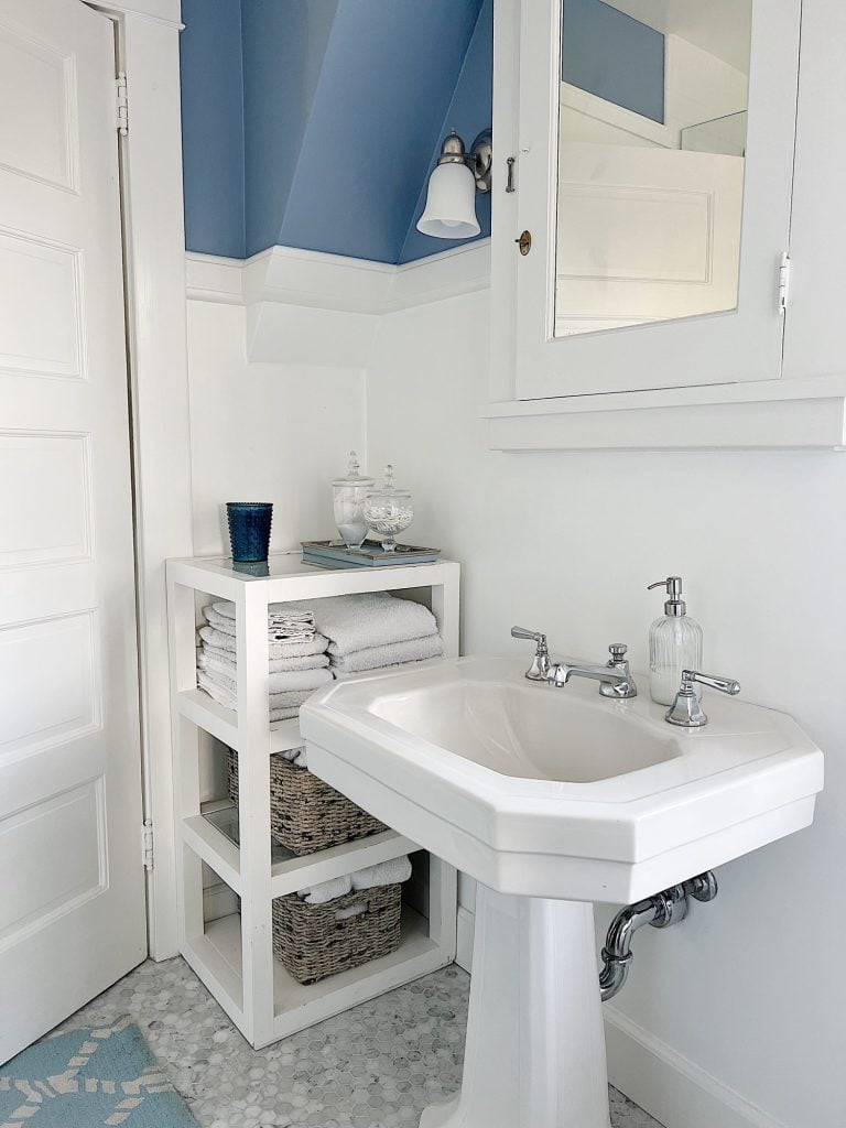 guest bathroom with white pedestal sink, cabinet with towels, apothecary jars with q-tips and makeup pads.