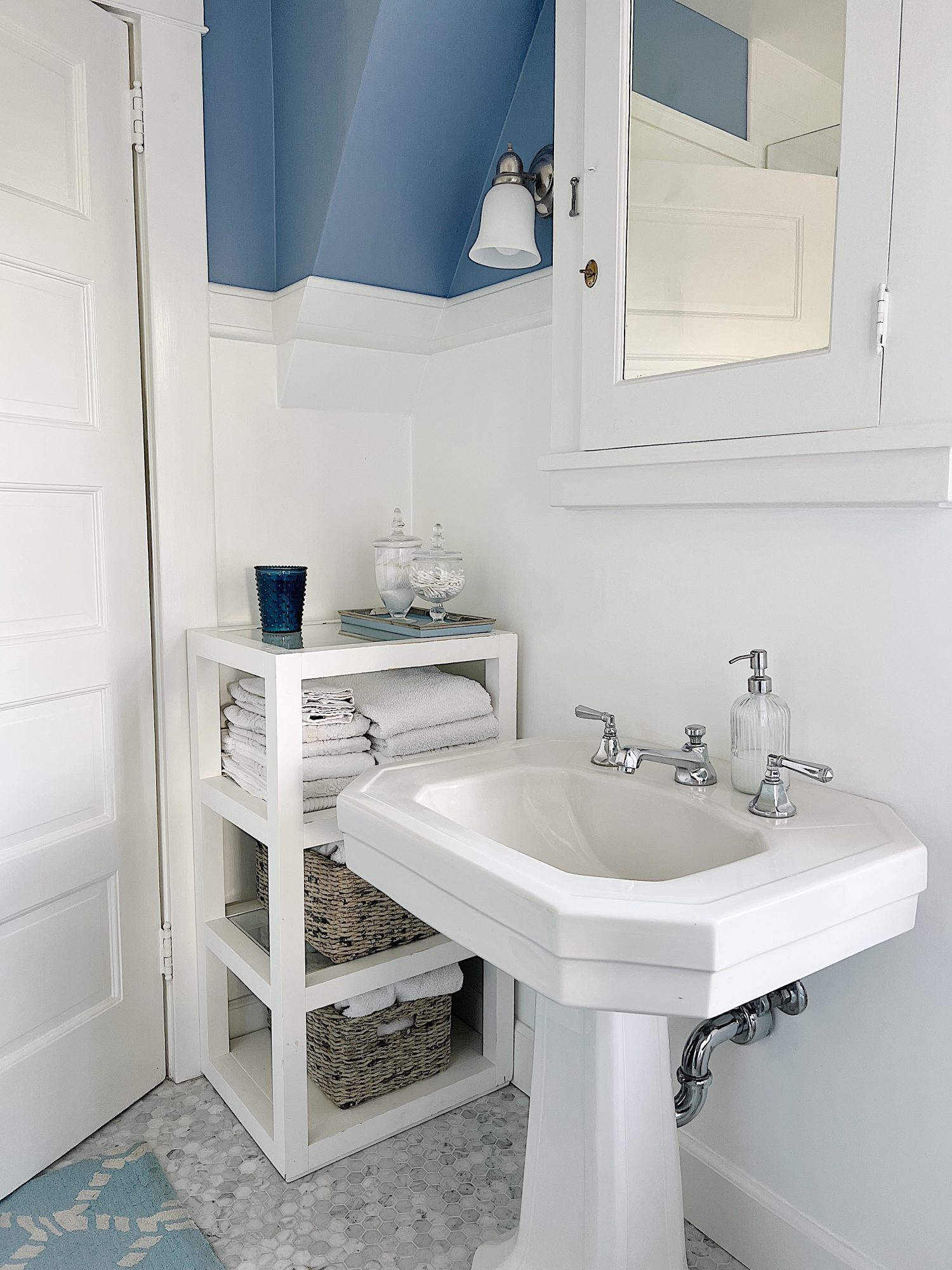 guest bathroom with white pedestal sink, cabinet with towels, apothecary jars with q-tips and makeup pads.