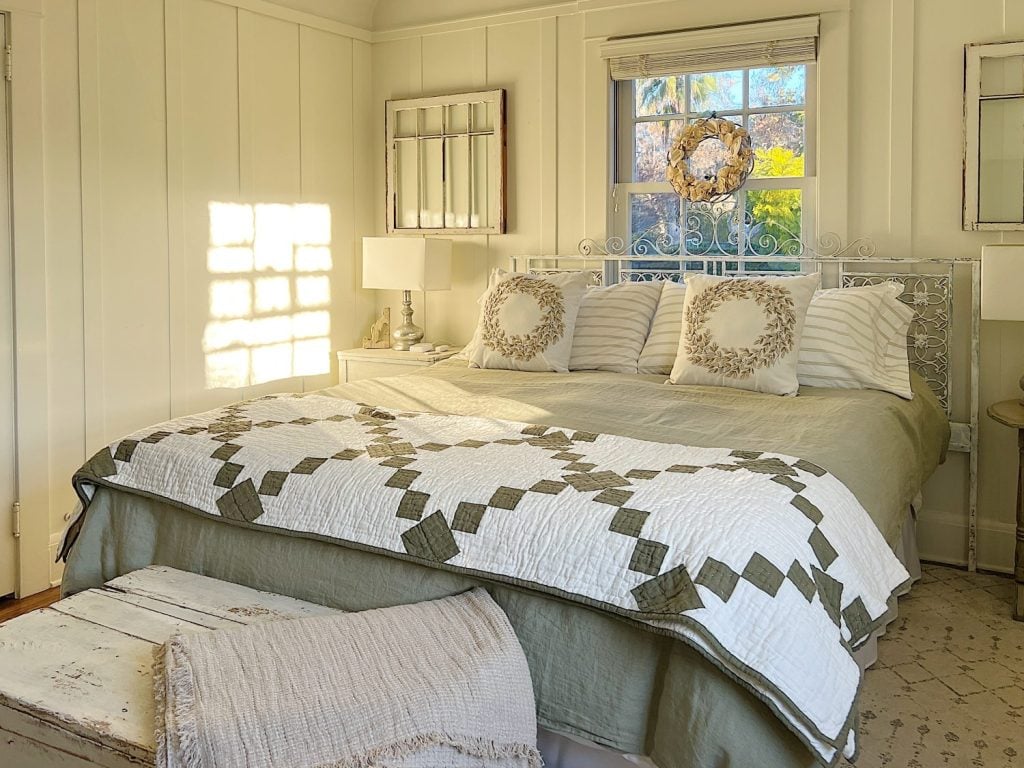 small bedroom with green linen duvet, green and white patchwork quilt, pillows and a nightstand on each side.
