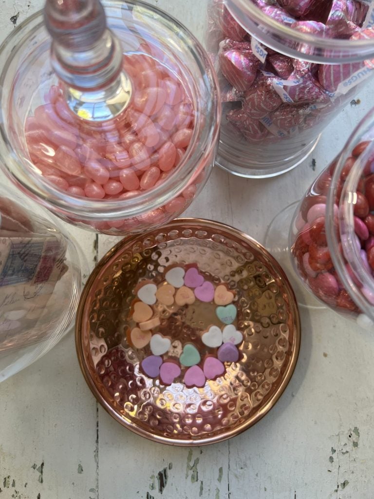 Top down view of apothecary jars filled with candy and small copper bowl with candy conversation hearts