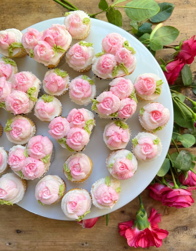 cupcakes decorated with white and pink buttercream frosting on a tray with flowers