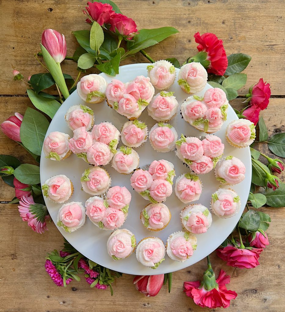 cupcakes decorated with white and pink buttercream frosting on a tray with pink flowers