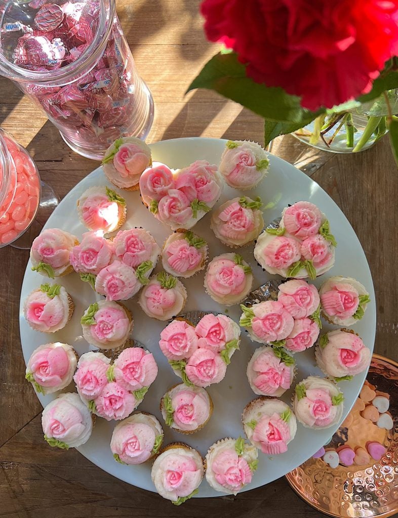 cupcakes decorated with white and pink buttercream frosting on a tray with flowers and candy