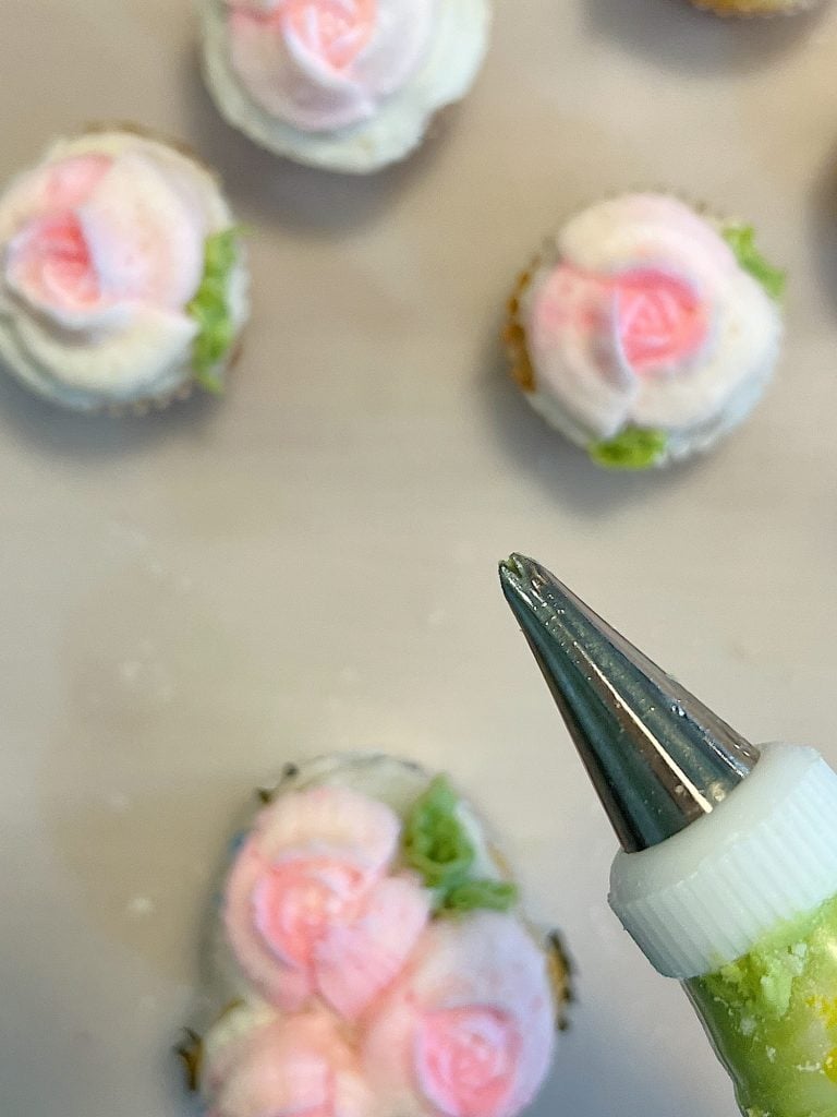 cupcakes decorated with white and pink buttercream frosting and green leaves