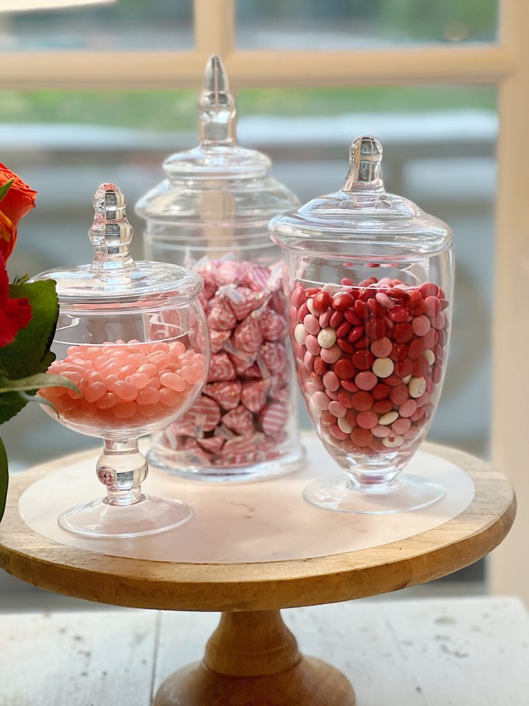 three glass apothecary jars filled with Valentine's Day candy.