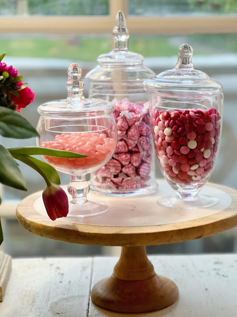 three glass apothecary jars filled with Valentine's Day candy.