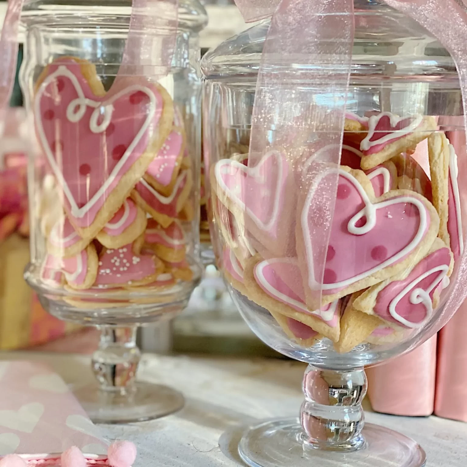 Valentine decorated sugar cookies in two glass apothecary jars.