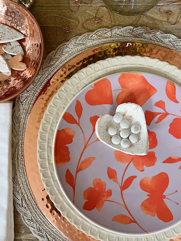 white clay hearts with copper foil cut into heartssitting on a valentine plate and a copper themed table setting.