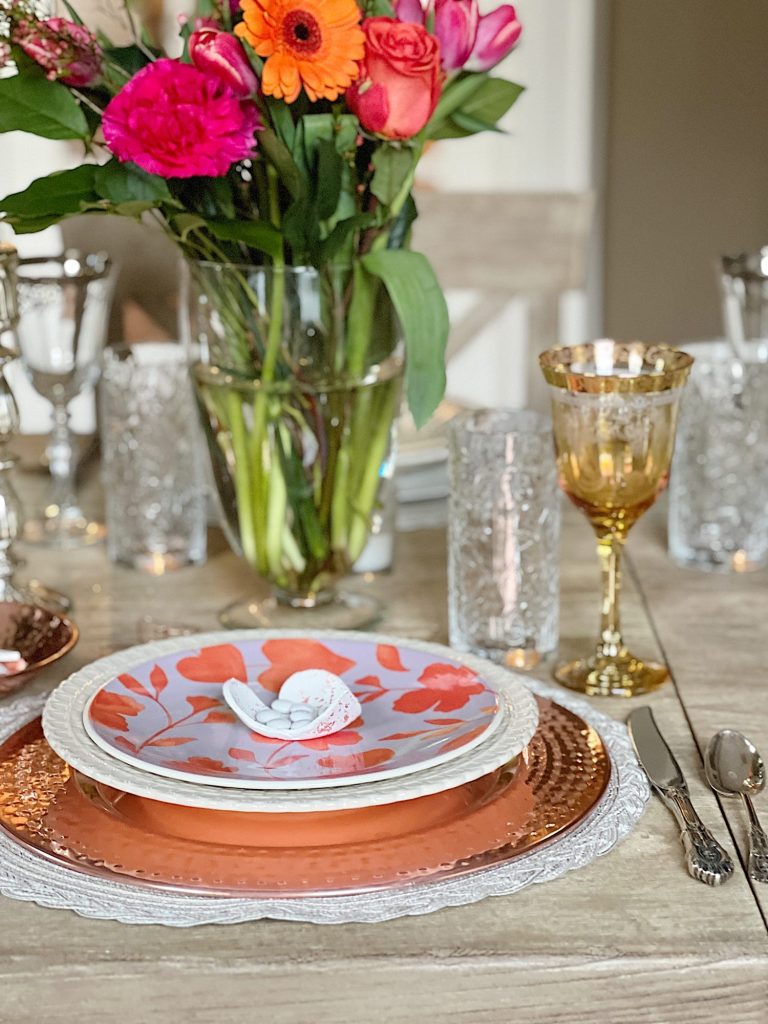 white clay hearts with copper foil cut into heartssitting on a valentine plate with an apothecary jar filled with fresh flowers and a copper themed table setting.