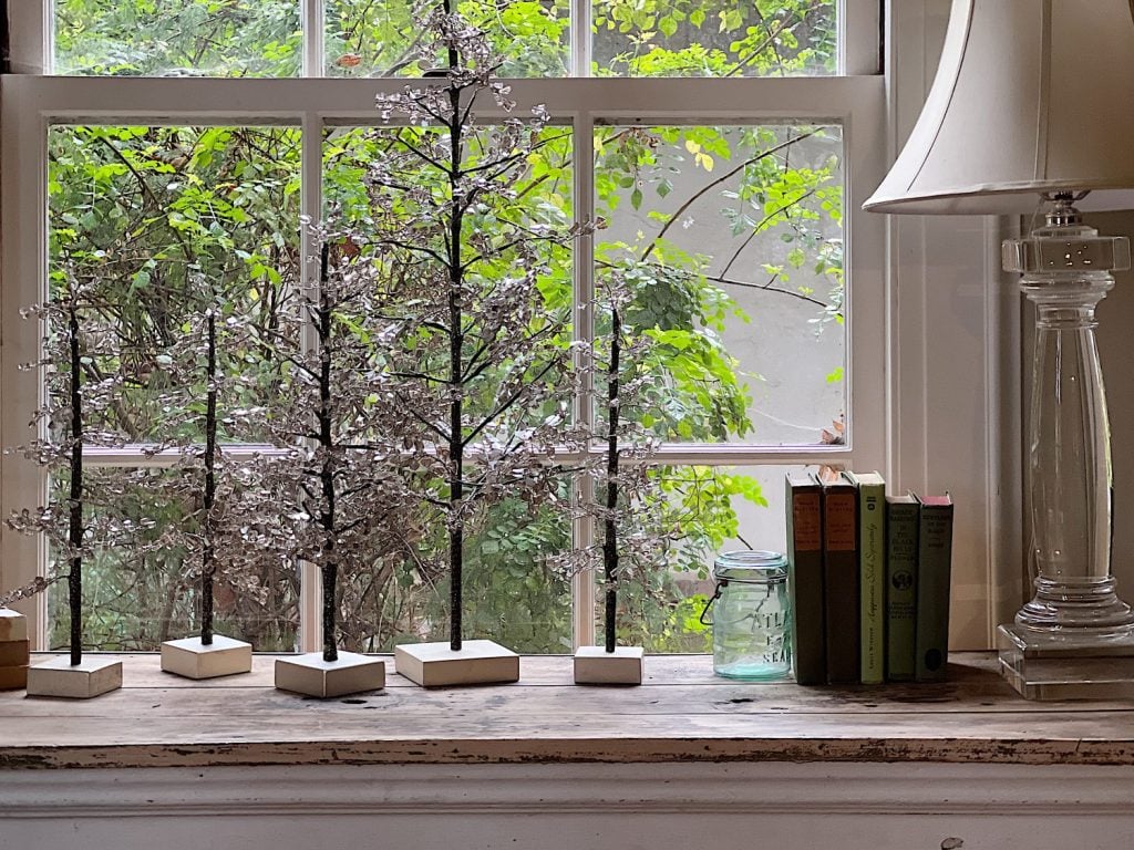 window with table with five glass trees, green books, glass lamp, and green vintage jar