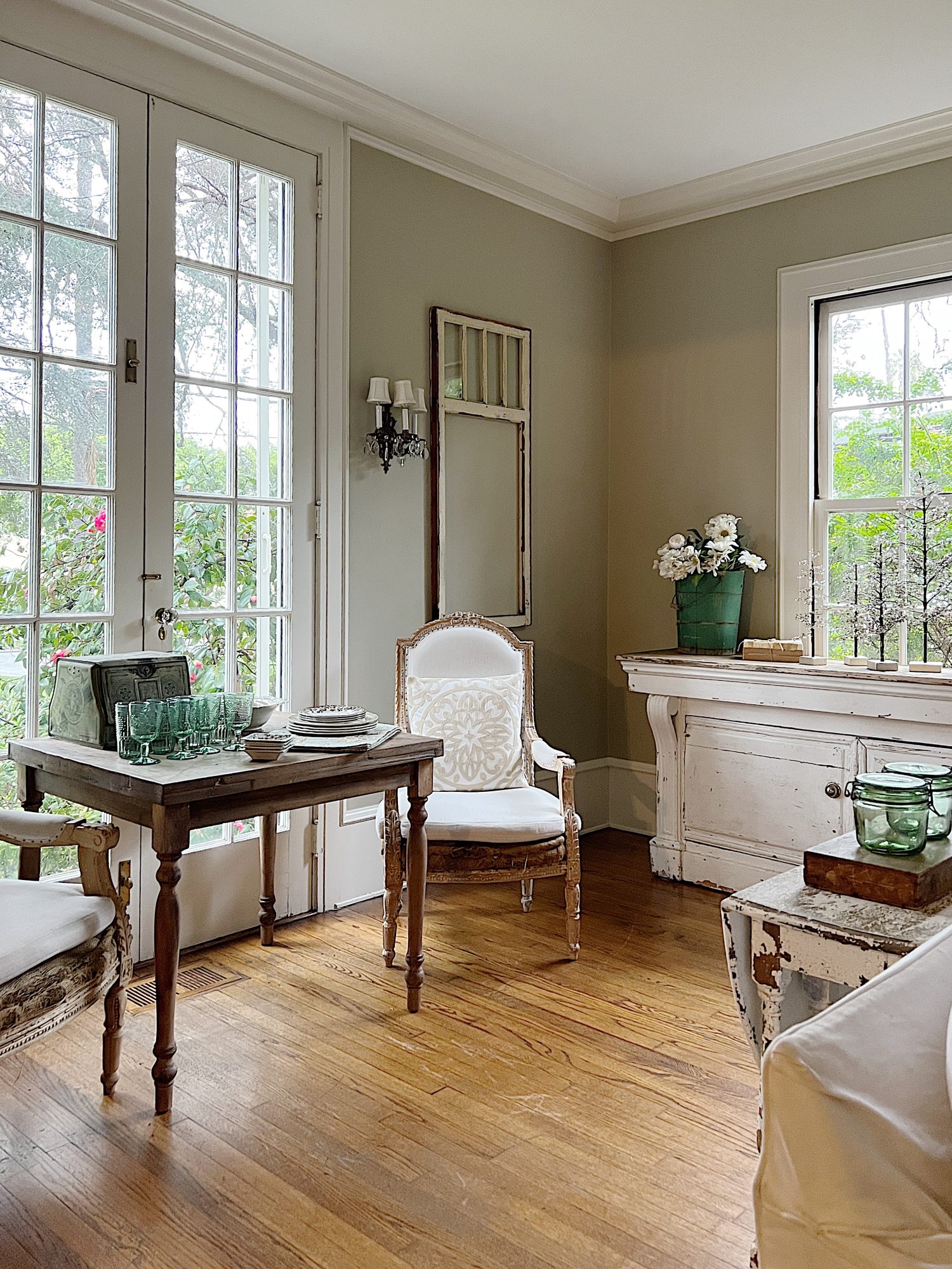living room with vintage counter, white couch, wood table with green glasses, vintage wood chair, and plates and bright window