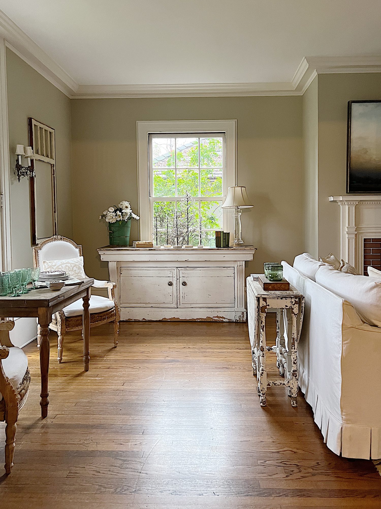 living room with vintage counter, white couch, wood table with green glasses, vintage wood chair, and plates and bright window