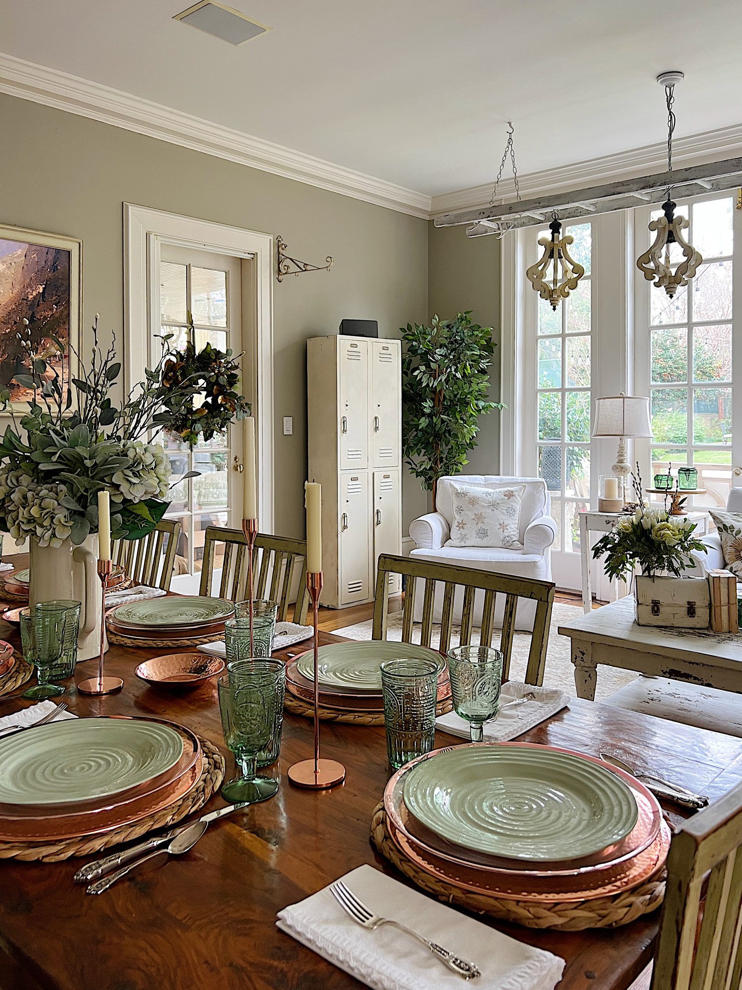 table set with hyacinth placemat, copper charger, green plate, green glasses, copper candlesticks, and green flowers in a vase. White chair in background.