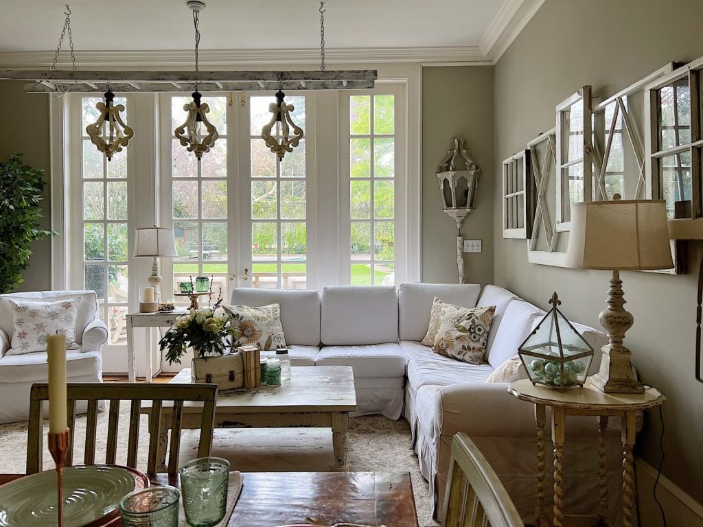 Family room with white chair and couch, hanging chandelier and decor items in sage green and taupe.