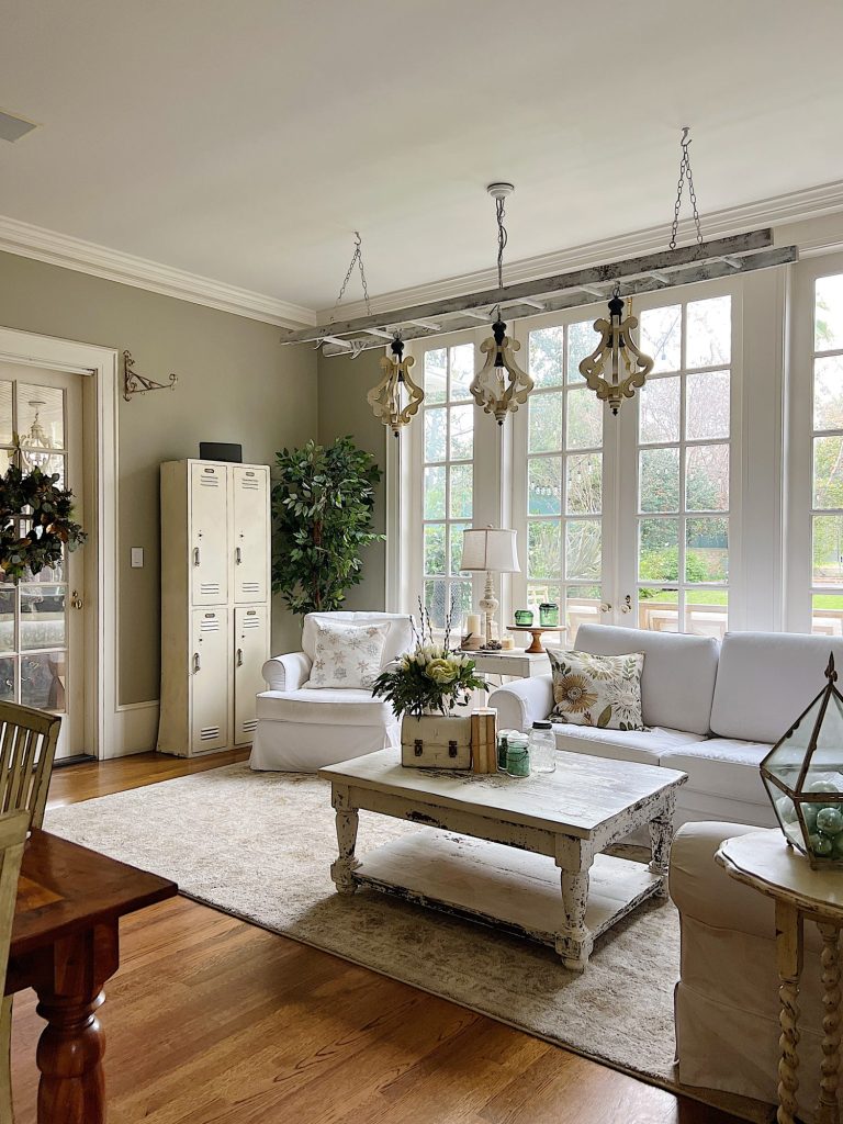 Family room with white chair and couch, hanging chandelier and decor items in sage green and taupe.