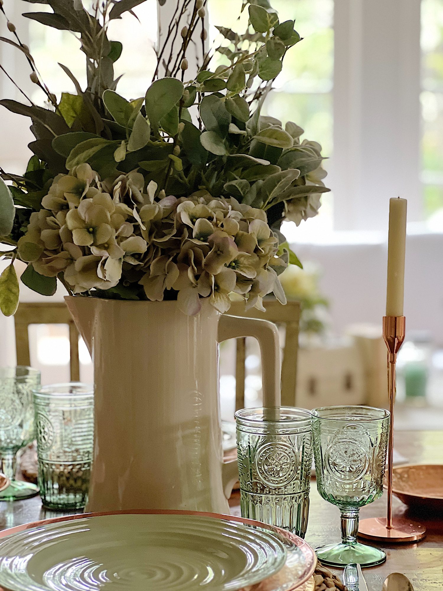 table set with hyacinth placemat, copper charger, green plate, green glasses, copper candlesticks, and green flowers in a vase.