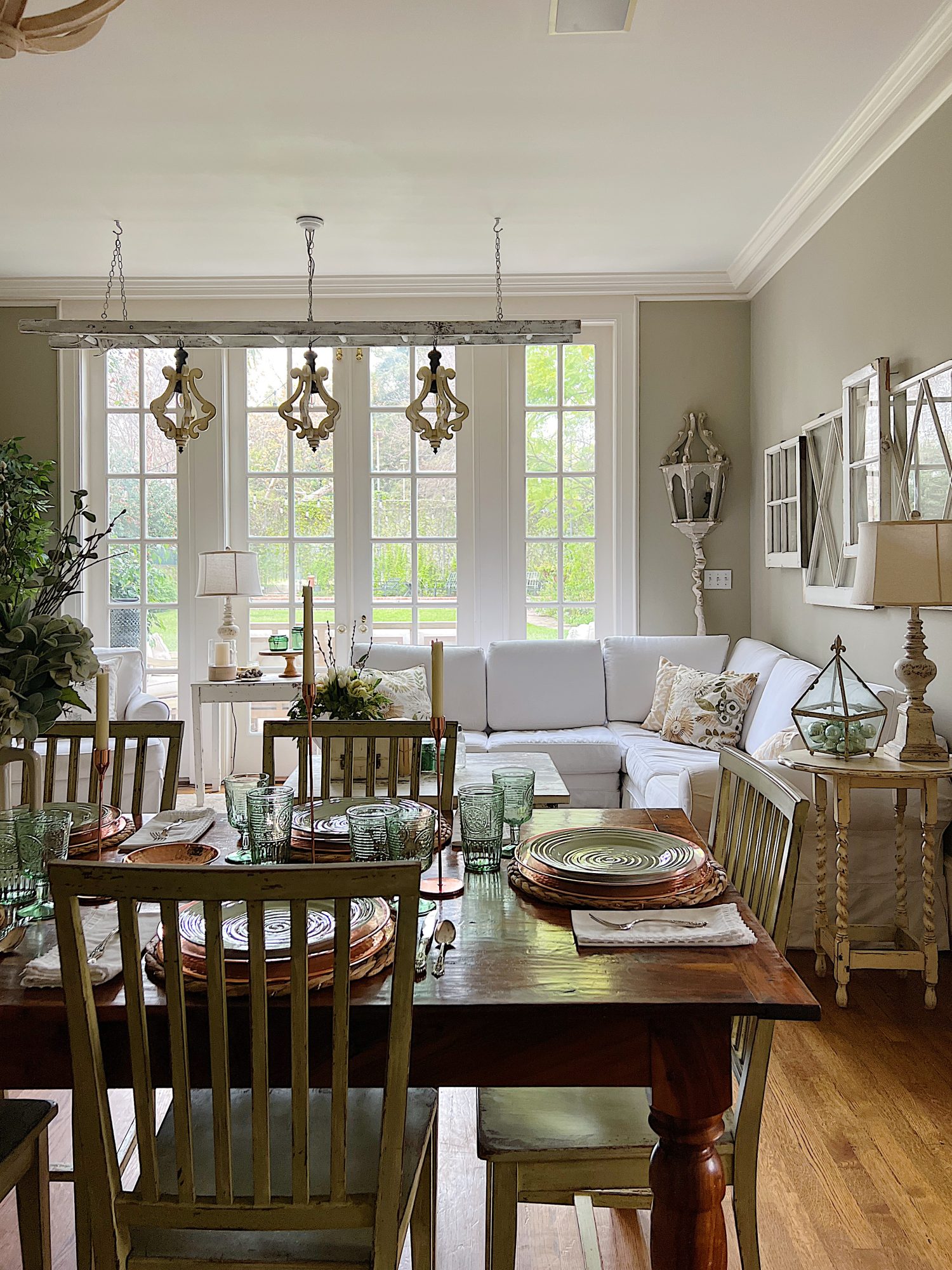 table set with hyacinth placemat, copper charger, green plate, green glasses, copper candlesticks, and green flowers in a vase. White couch in background.