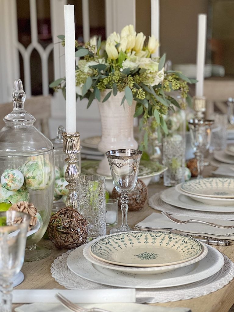 table with green palce settings and apothecary jars with green apples, wood balls, silver goblets, and decor balls