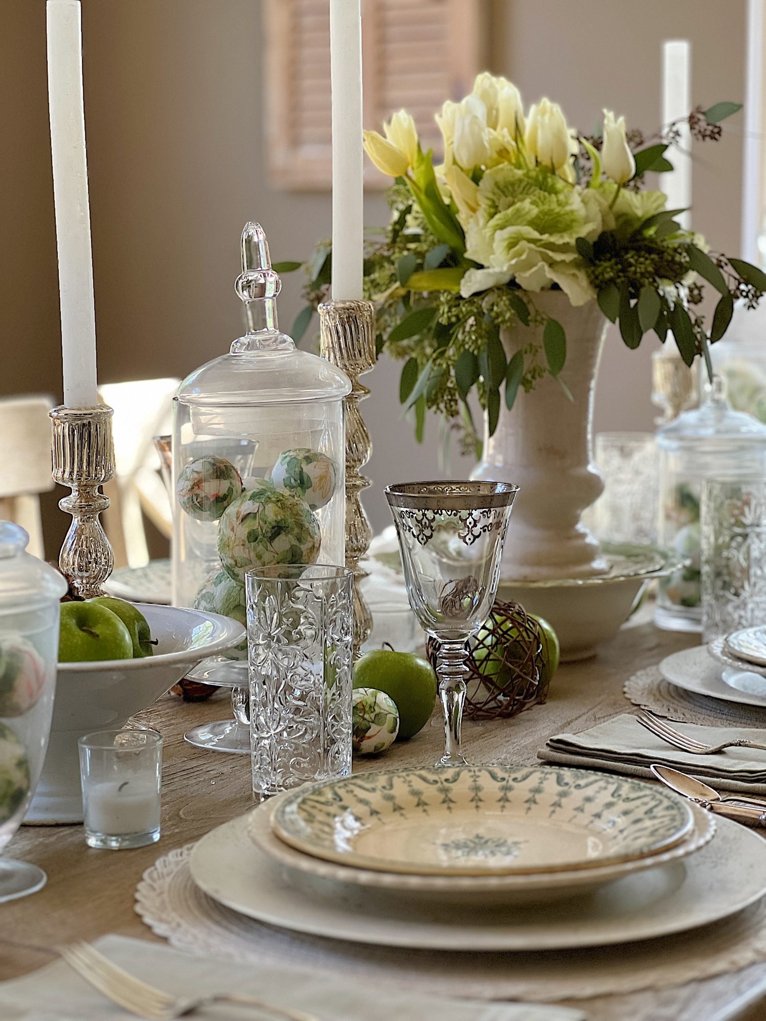 table with green palce settings and apothecary jars with green apples, wood balls, silver goblets, and decor balls