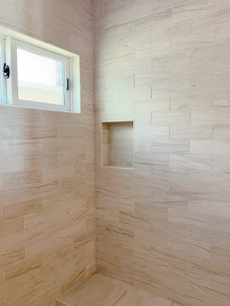 Primary bathroom shower with tan marble tile