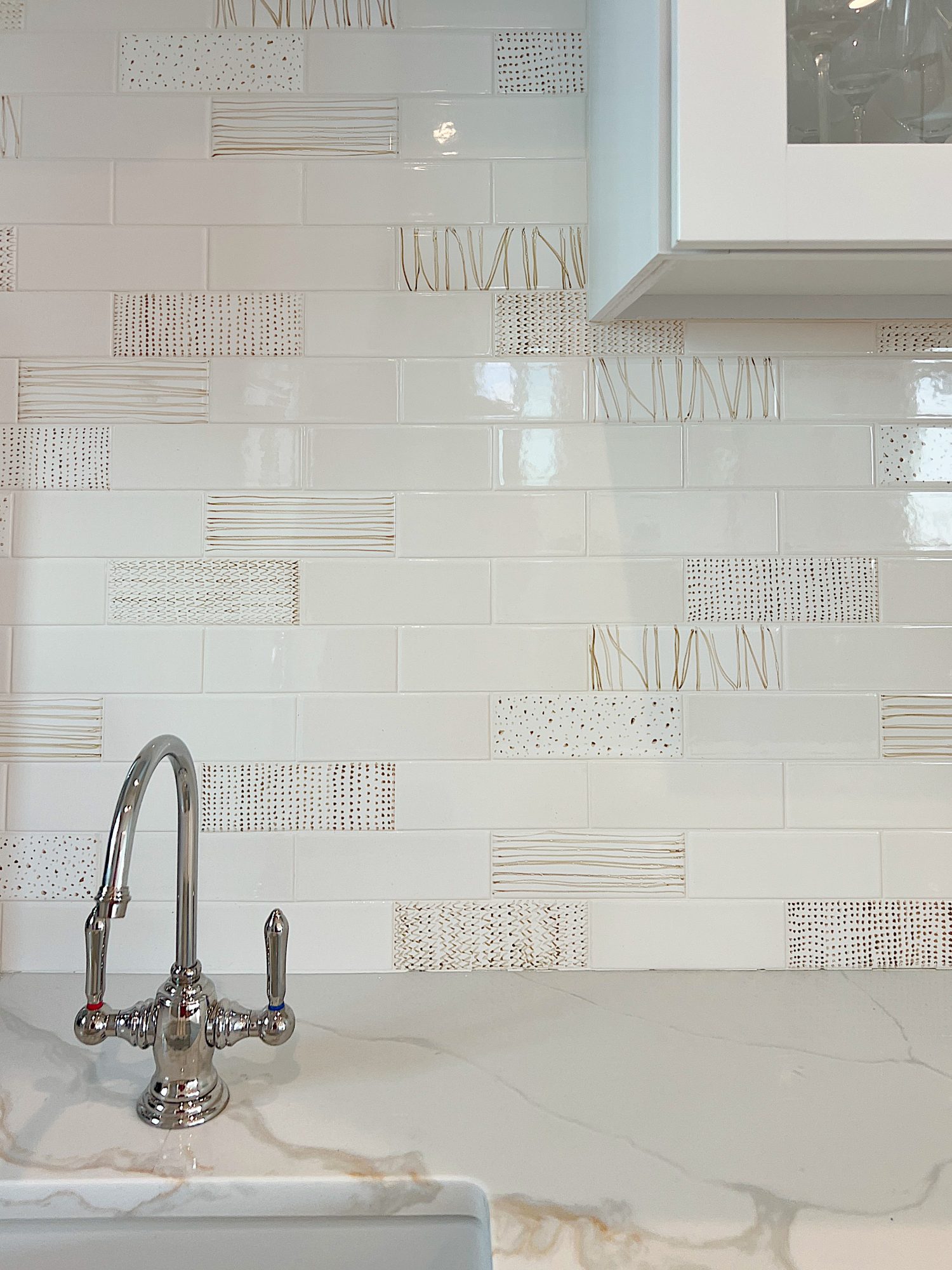 Beverage side of the kitchen with hand painted tiles, water dispenser, quartz countertops and white cabinets.