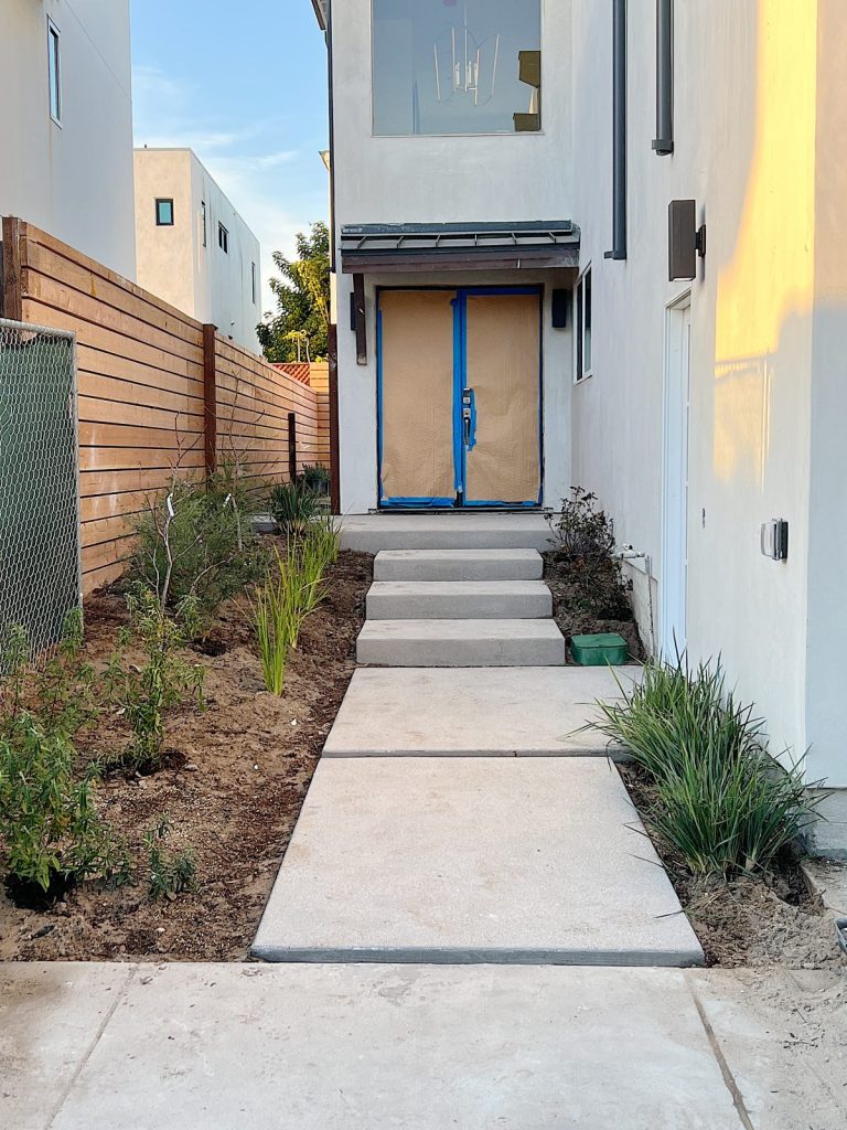 Front walkway at the beach house with new concrete pads, landscaping, and front doors (hidden behind paper).