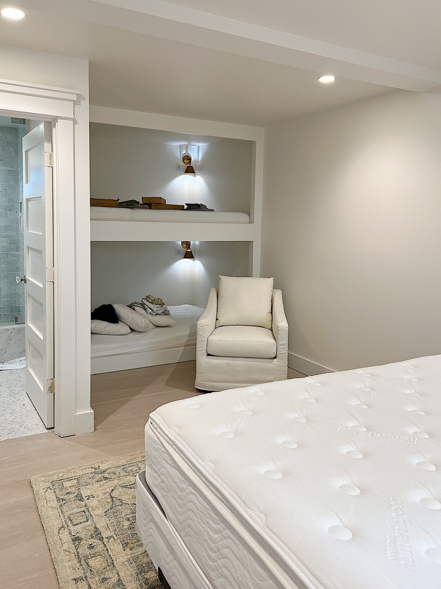 A bedroom with two queen bunks, a king sized bed, and a bathroom.There is also a swivel rocker chair.