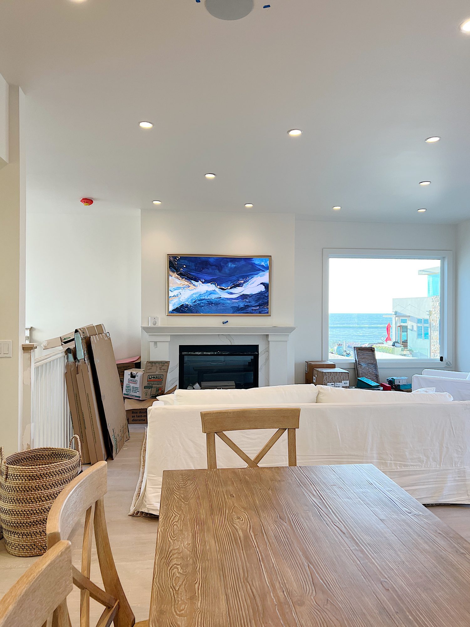 Living area of the newly remodeled beach house with fireplace, TV, coffee table, rug and white sofa. Table and kitchen island are in the foreground.