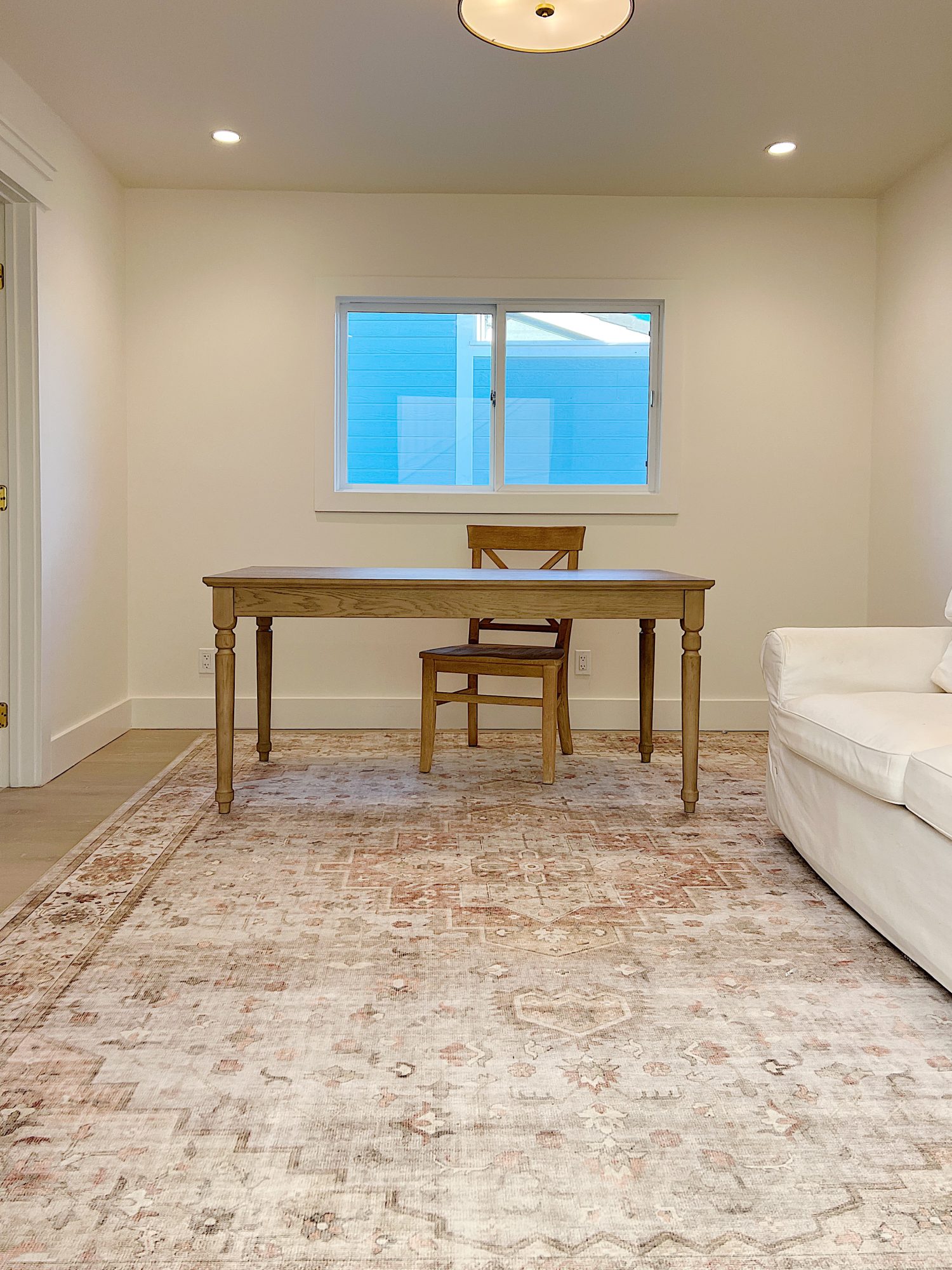 New office in our brach house with rug, wood desk, white sofa bed.