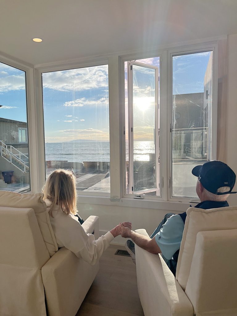 Me and my husband sitting in our new primary bedroom in reclining chairs facing windows with ocean view.