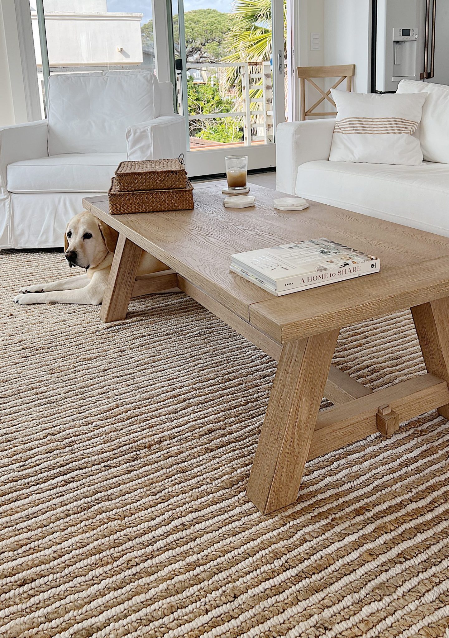 tan wood coffee table in a white living room with white couch and chair and a striped rug