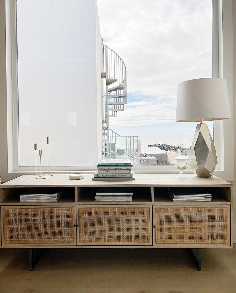 a rattan media console sitting in front of a large window with a view of the ocean