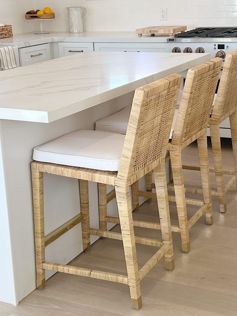 Three rattan stools with white cushions at a kitchen island