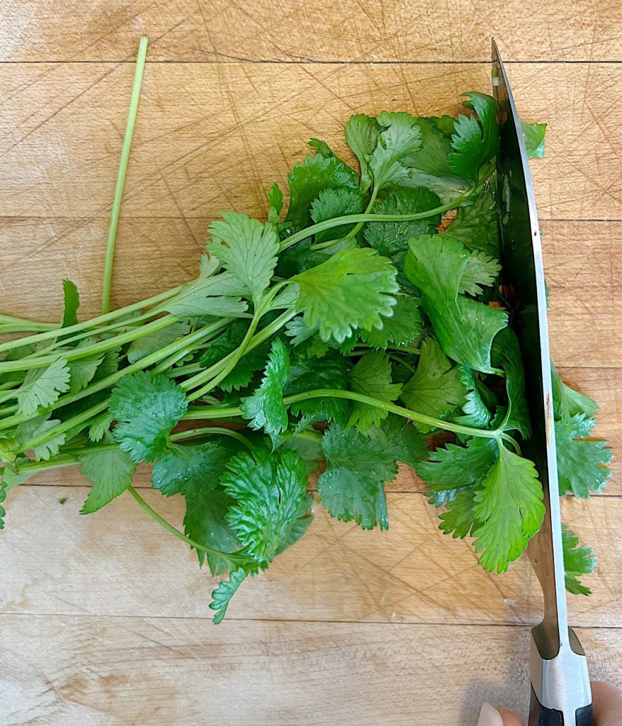 chopping cilantro on a cutting board with a knife
